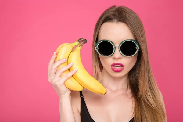 Primer plano de la joven hembra en gafas sosteniendo plátanos — Foto de Stock