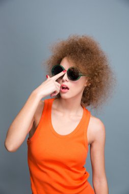 Amusing pretty curly female posing and fixing sunglasses