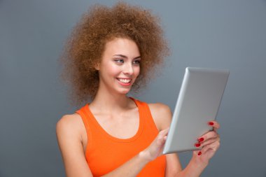 Joyful smiling curly young female using tablet