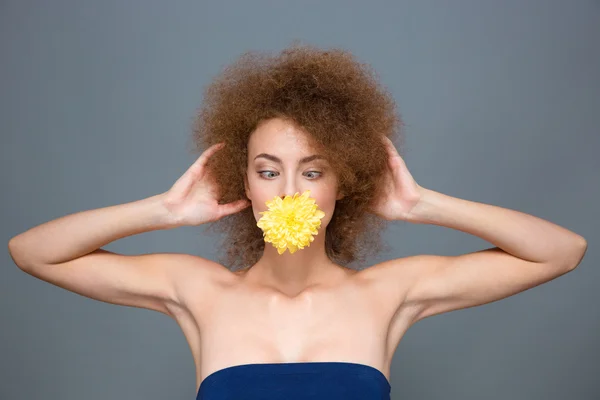 Underhållande curly girl med blomma i munnen skojar och skelning — Stockfoto