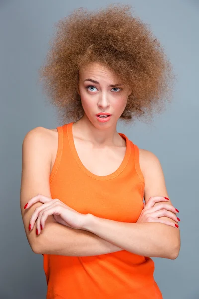 Belle jeune femme bouclée choquée et posant avec les bras croisés — Photo