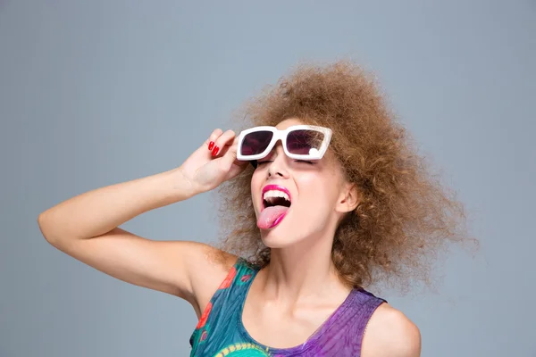 Funny curly woman in sunglasses with eyes closed showing tongue — Stock Photo, Image