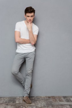 Thoughtful young guy standing on gray background