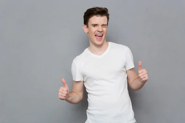 Happy young man giving thumbs up sign and winking — Stock Photo, Image