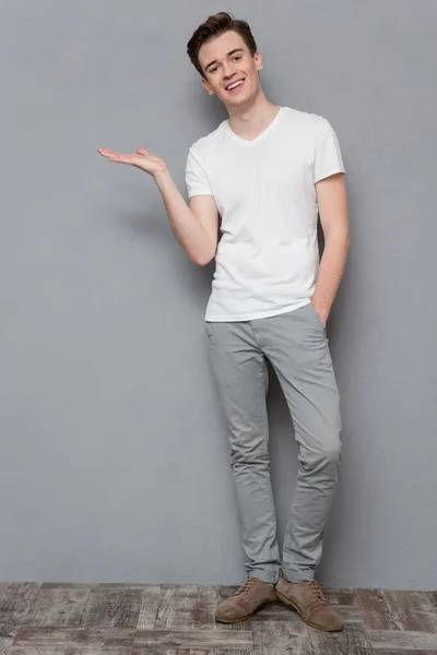 Happy young man holding copyspace on palm over gray background — Stock Fotó