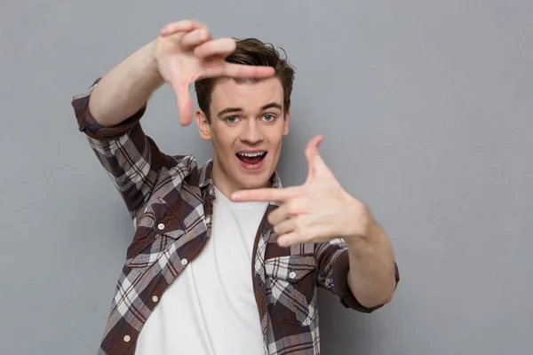 Joyful handsome young man making frame with fingers — Stockfoto