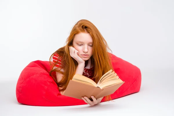 Concentrated girl relaxing in red bean bag and reading book — Stockfoto