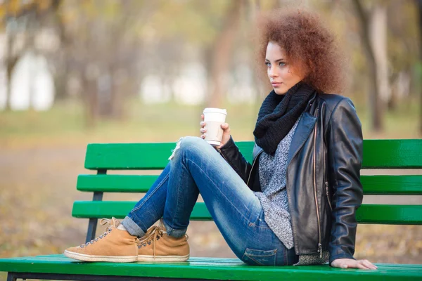 Mujer sentada en el banco y sosteniendo la taza con café —  Fotos de Stock