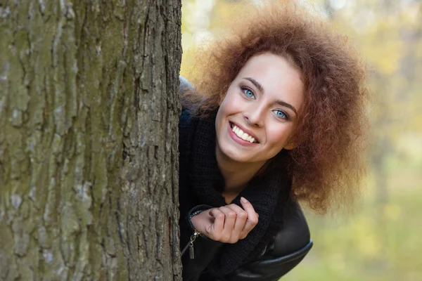 Mujer con el pelo rizado asomándose por detrás de un árbol — Foto de Stock