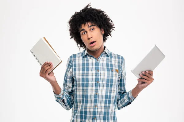 Afro american man choosing between paper book or tablet computer — ストック写真