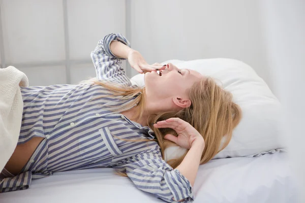 Joven mujer bonita bostezando y estirándose acostada en la cama —  Fotos de Stock