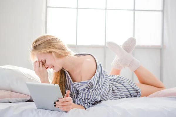 Malu wanita lucu berbaring di tempat tidur dan menggunakan tablet — Stok Foto