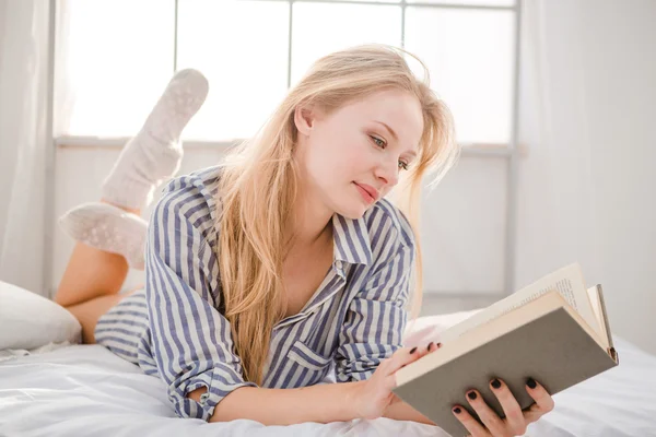 Mujer rubia tierna acostada en la cama y leyendo libro —  Fotos de Stock