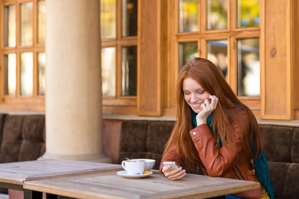 Cute smiling female using smartphone in outdoor cafe — ストック写真