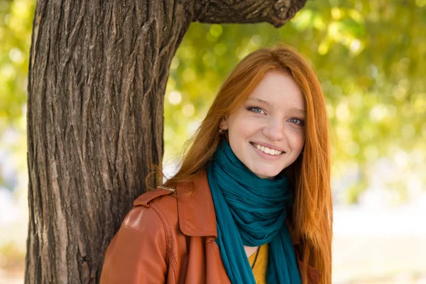 Jovem mulher sorridente posando perto da árvore no parque — Fotografia de Stock