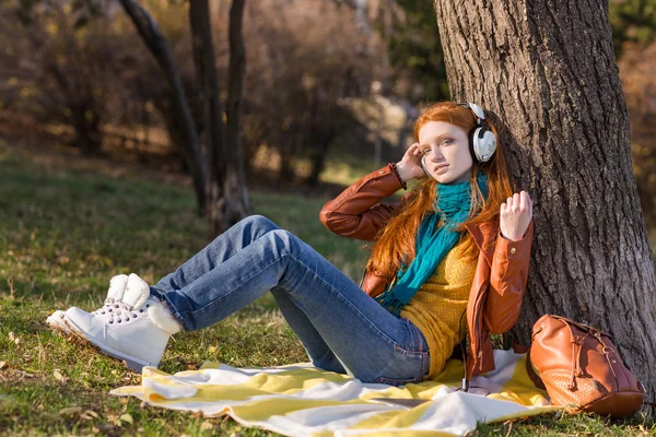 Atraente senhora relaxada ouvindo música sentada debaixo da árvore — Fotografia de Stock