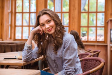 Kafede oturan ve kameraya bakan kadın.