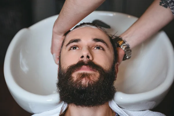 Cabeça de lavagem cabeleireiro do homem com barba na barbearia — Fotografia de Stock