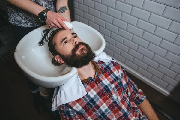 Frisör tvätta håret på ung man med skägg — Stockfoto