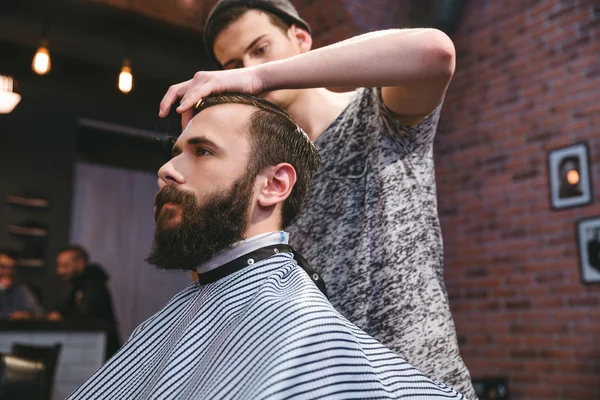 Jovem barbeiro corte de cabelo de hipster barbudo na barbearia — Fotografia de Stock