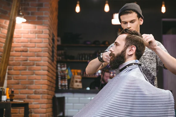 Joven peluquero haciendo corte de pelo de hombres a un hombre barbudo — Foto de Stock