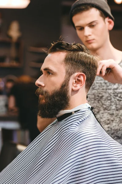 Профессиональный парикмахер стрижет бородатого мужчину — стоковое фото