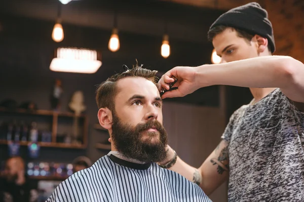 Peluquero hábil corte de pelo de hombre joven con barba — Foto de Stock