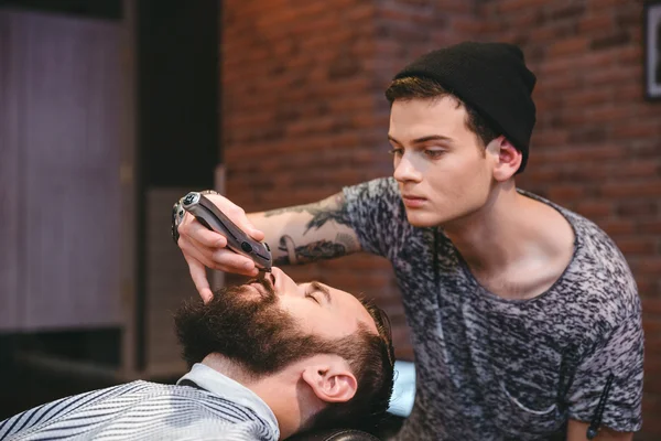 Koncentrerad frisör trimma skägget av stilig man i barbershop — Stockfoto