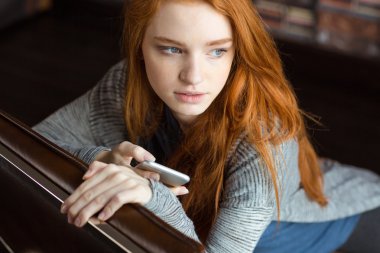 Oturma ve cep telefonu tutan çekici düşünceli genç kadın