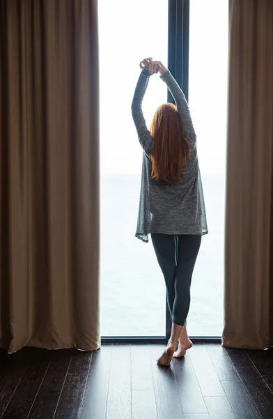 Atractiva dama delgada de pie y estirándose en la ventana grande —  Fotos de Stock