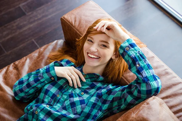 Hermosa mujer alegre acostada en un sofá marrón y riendo —  Fotos de Stock