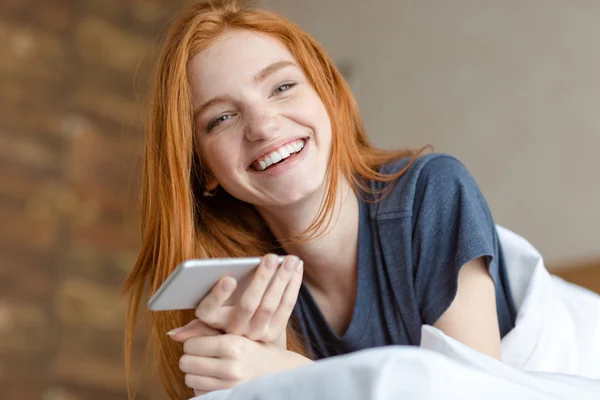 Redhead woman lying on the bed with smartphone — Stock Photo, Image
