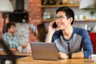 Dizüstü bilgisayar kullanarak ve telefonda konuşurken olumlu Asyalı adam