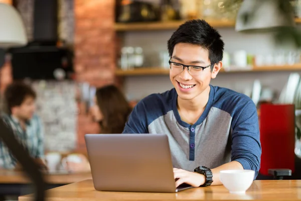 Feliz alegre asiático macho sonriendo y utilizando el ordenador portátil en la cafetería —  Fotos de Stock