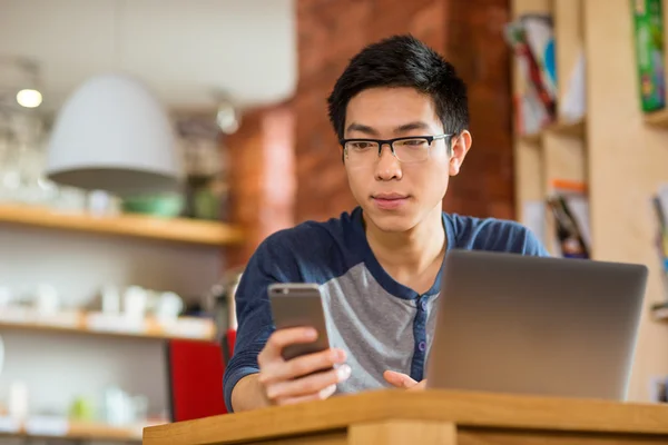 Продуманий азіатський чоловік використовує смартфон і ноутбук — стокове фото