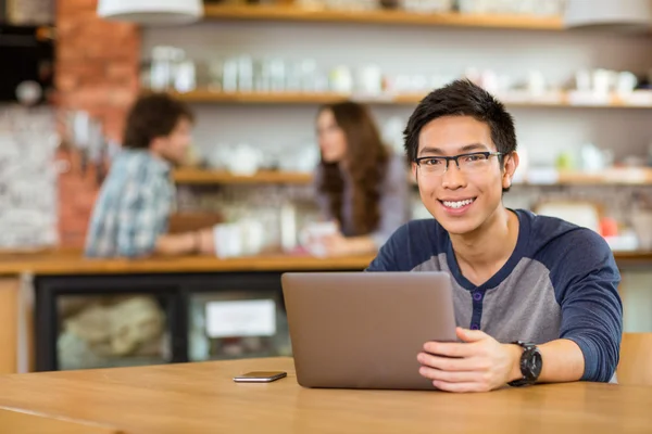 Jovem alegre asiático homem em óculos usando laptop — Fotografia de Stock