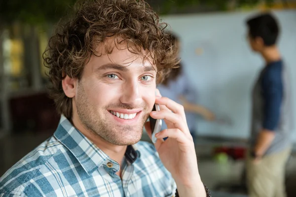Веселий чоловік розмовляє на мобільному телефоні під час роботи своєї команди — стокове фото