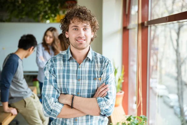 Attractive positive male with folded hands standing near the window — Stock Photo, Image