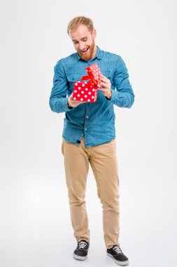 Cheerful joyful young blond bearded man opening gift