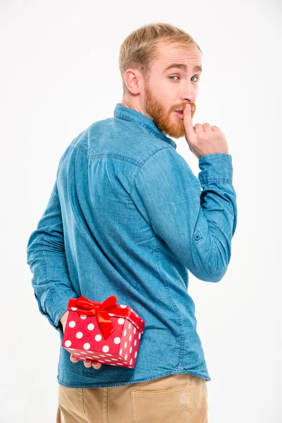 Handsome  man hiding gift behind back and gesturing silence — Stock Photo, Image