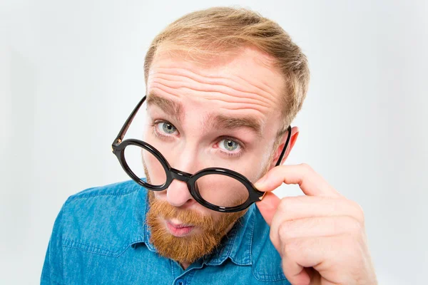 Amusing young man with beard looking over black round glasses — Stockfoto