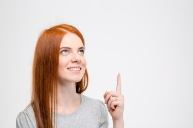 Excited smiling beautiful girl with long red hair pointing up 