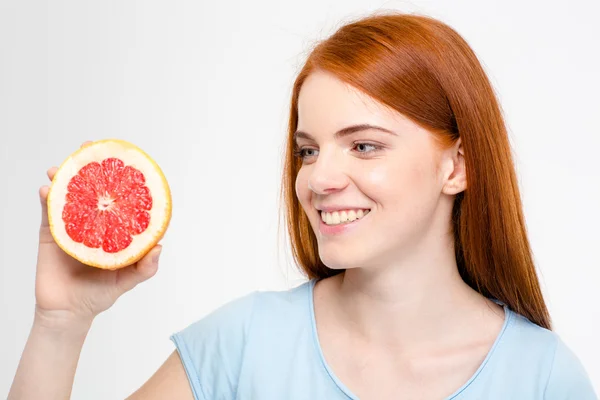 Smiling young happy redhead female looking on half of grapefruit — Zdjęcie stockowe