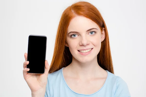 Charming cheerful young redhead woman showing blank screen of smartphone — Stock fotografie