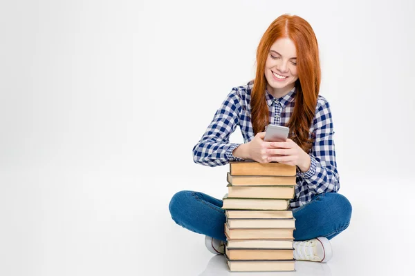 Mujer positiva sentada cerca de la pila de libros y usando el teléfono celular — Foto de Stock