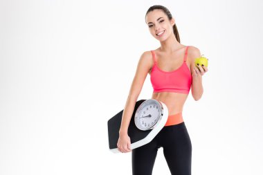 Cheerful beautiful fitness woman holding weighing scale and yellow apple