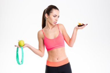 Woman holding apple, mesuring tape and cake making a choice