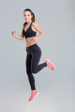 Cheerful active young sportswoman in fitness wear running 