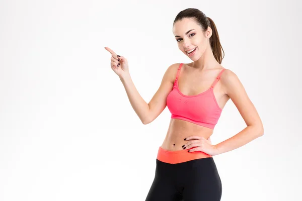 Cheerful attractive young fitness woman pointing away — Stock fotografie