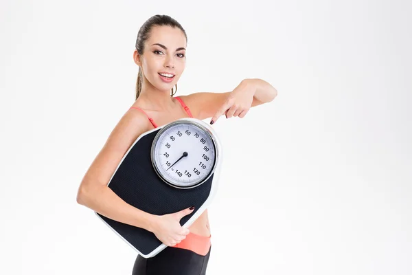 Pretty fitness girl holding weighing scale and pointing on it — 스톡 사진
